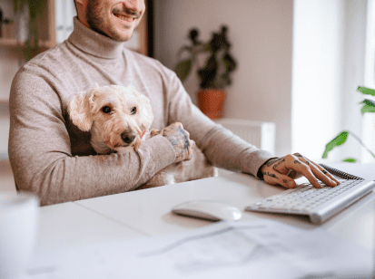 A man working whilst holding his small dog on his lap