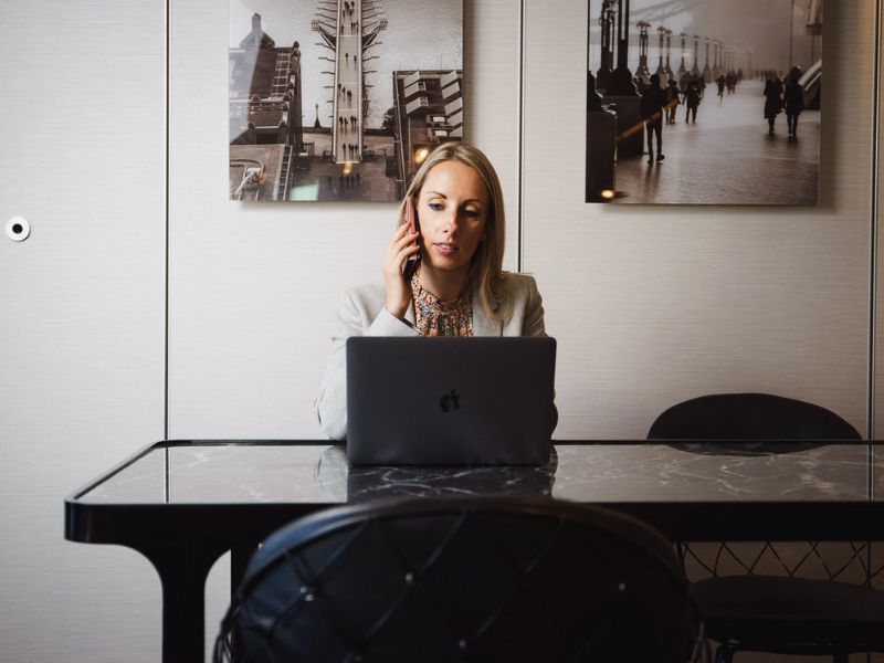 A female sitting at a table on her laptop and chatting on a mobile phone call.